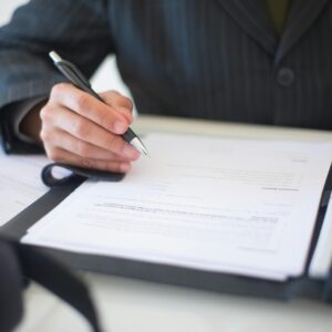 Close-up of a hand signing documents with a pen, symbolizing an important business contract.
